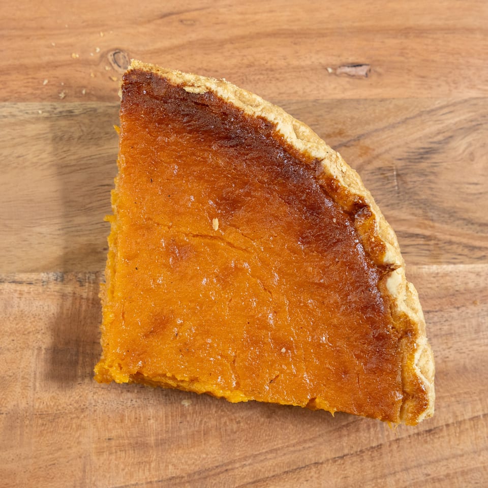 A slice of golden-brown custard pie with flaky crust rests on a wooden tabletop.