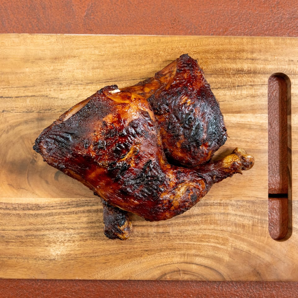 Whole roasted chicken with crisp, darkly glazed skin resting on a wooden cutting board.