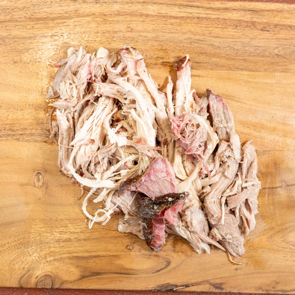 Shredded roasted meat with browned and pink pieces arranged on a wooden cutting board.