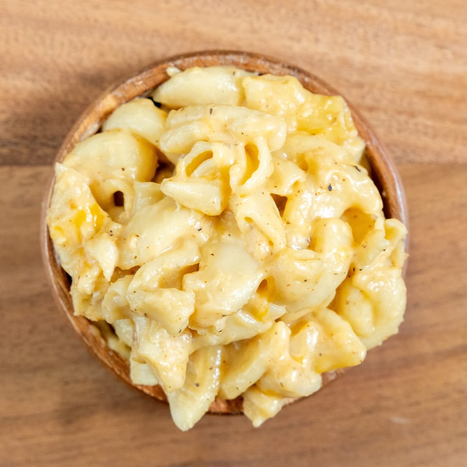 Overhead view of creamy cheese-coated pasta in a rustic bowl on a wooden table.