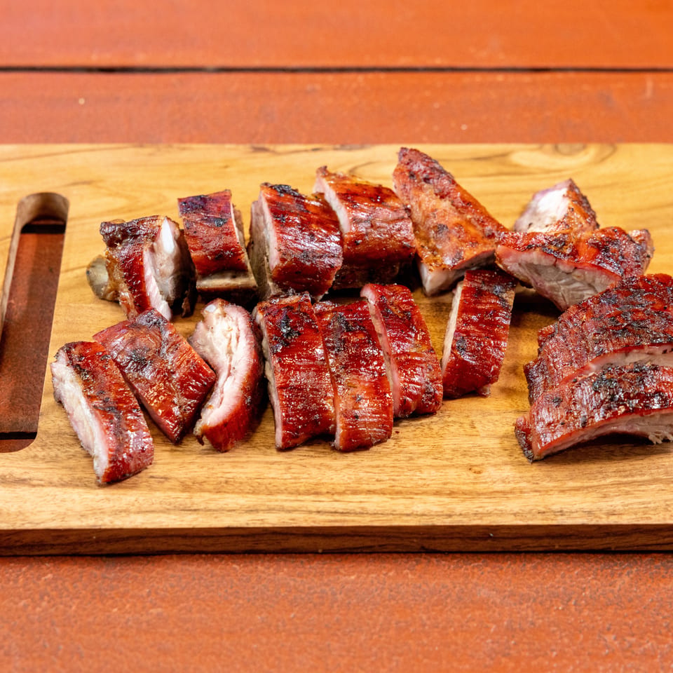 Sliced, charred ribs arranged on a wooden cutting board atop a rustic table.