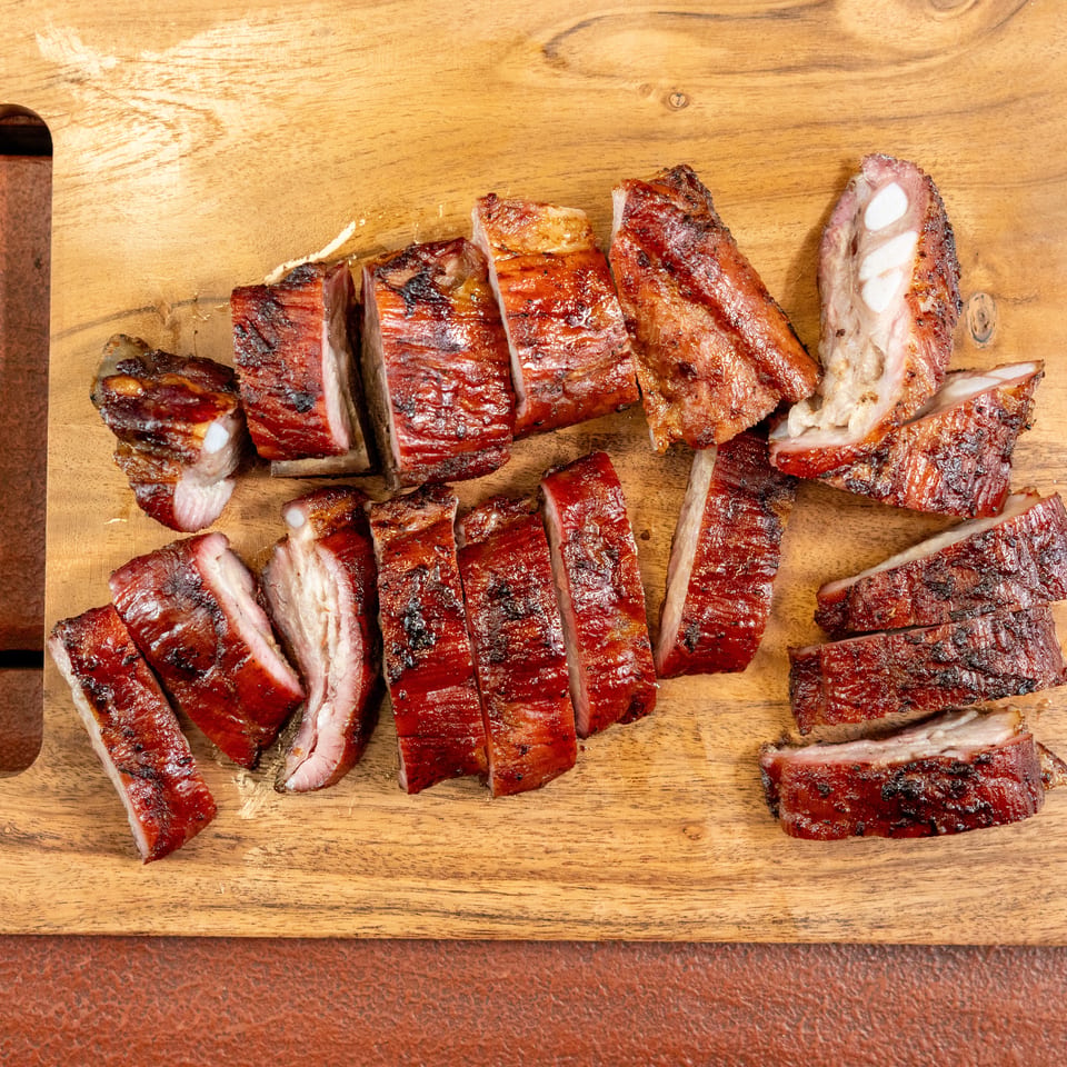Sliced, glazed barbecued ribs arranged across a rustic wooden serving board.