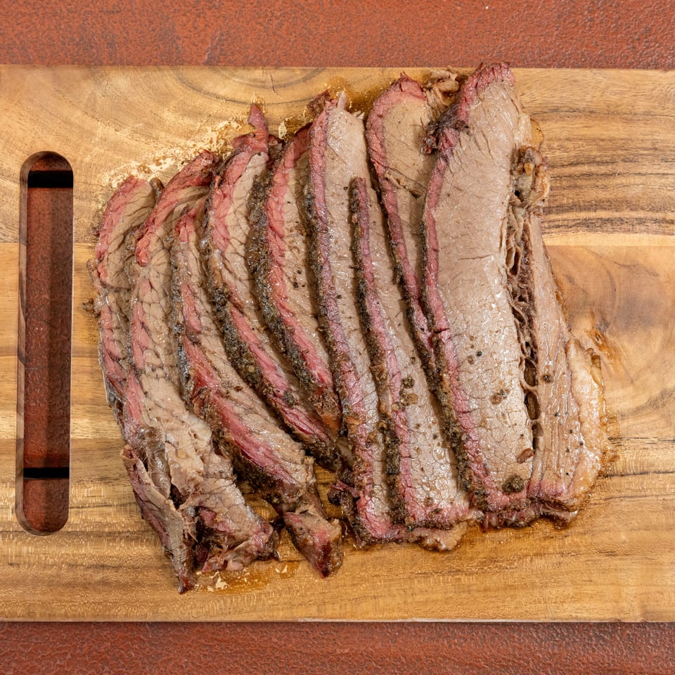 Sliced smoked beef brisket arranged on a wooden cutting board, showing browned edges and pink, juicy centers.