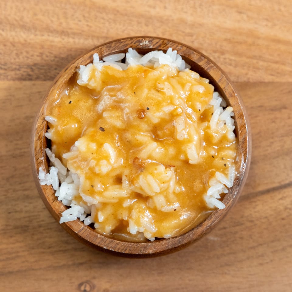 White rice topped with creamy orange curry sauce in a rustic wooden bowl on a wooden table.