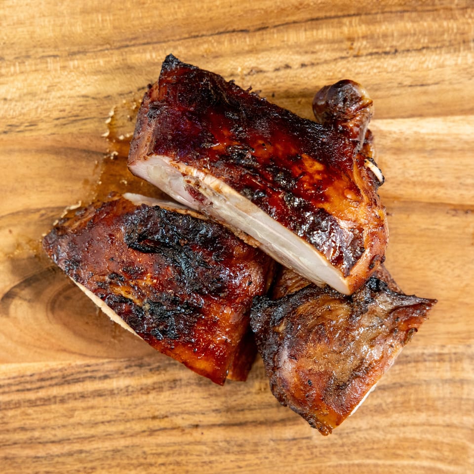 Smoky, charred slices of glazed barbecue meat stacked on a wooden cutting board.